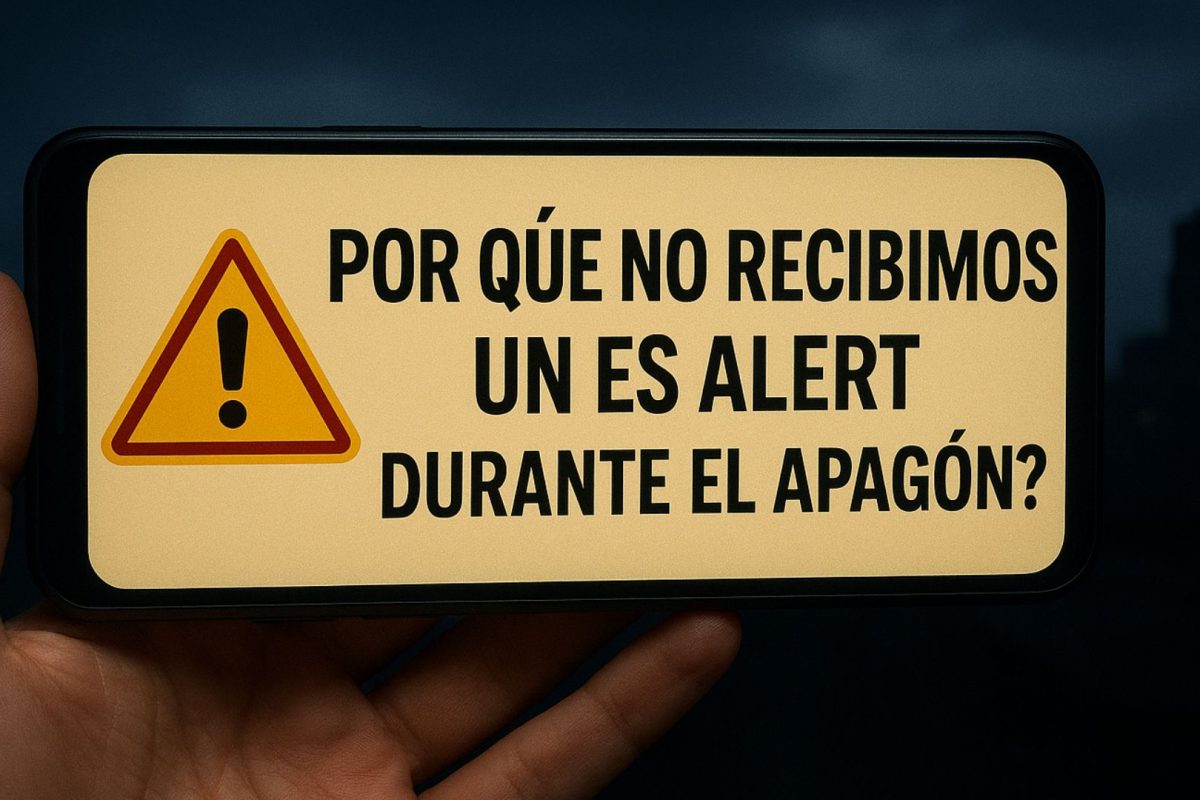Teléfono móvil mostrando una alerta de emergencia con el mensaje “¿Por qué no recibimos un ES Alert durante el apagón?”, sostenido por una mano frente a un fondo urbano oscuro.